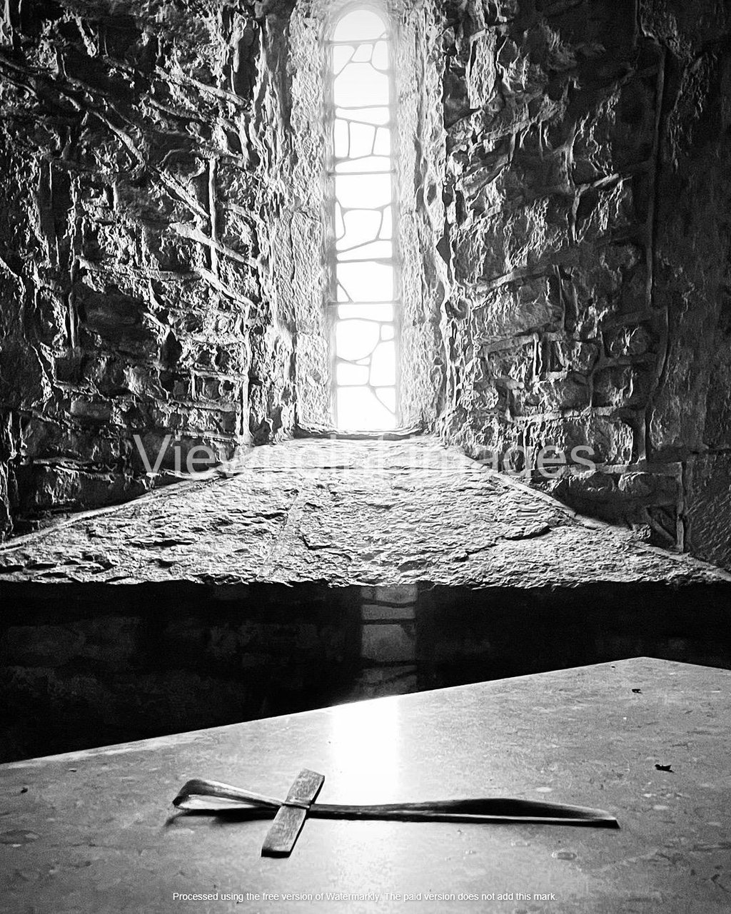 Black and white photo of a small stone cross on an altar inside a medieval castle window.