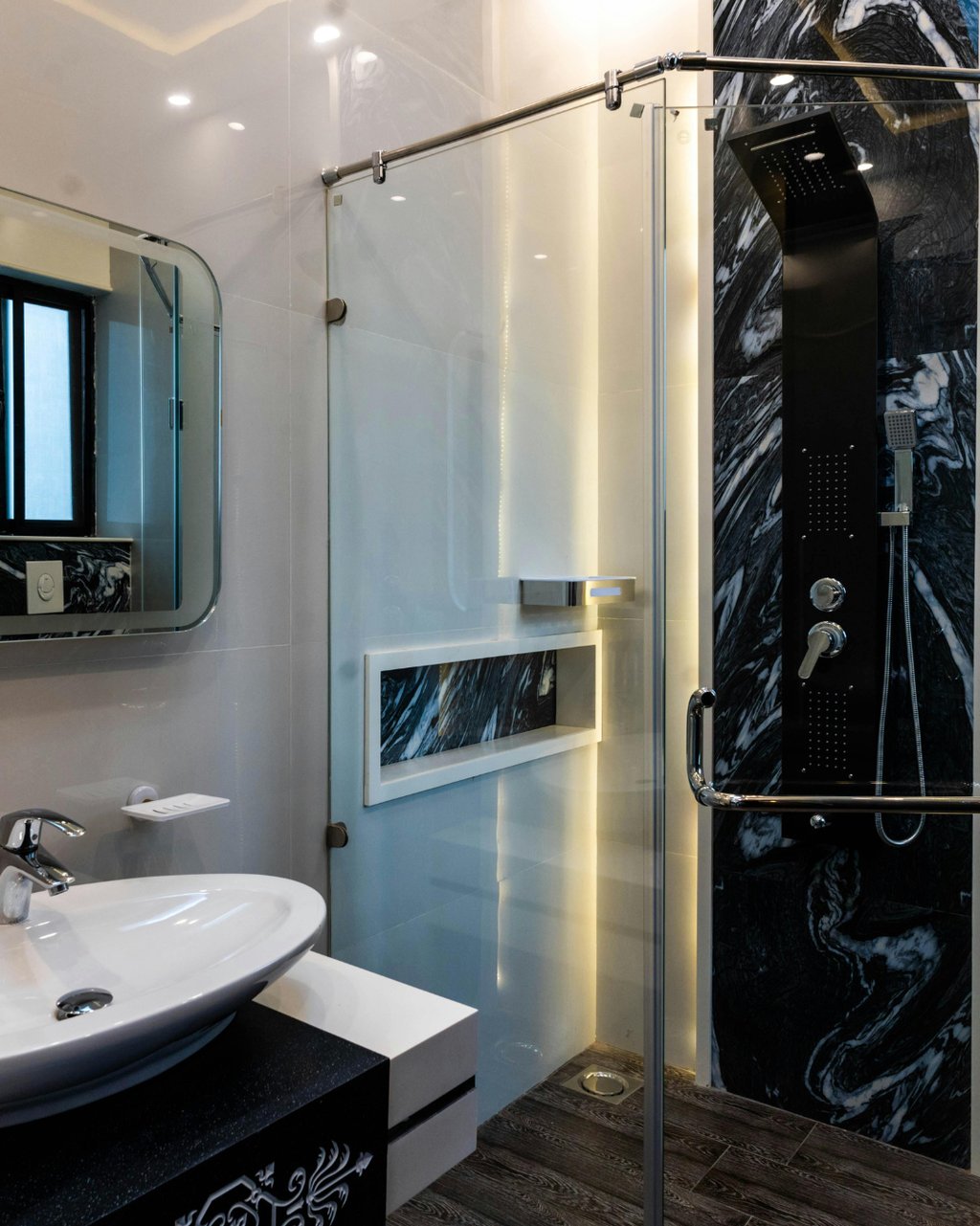 Baño reformado en Valencia con detalles en mármol negro, ducha de cristal y diseño elegante.