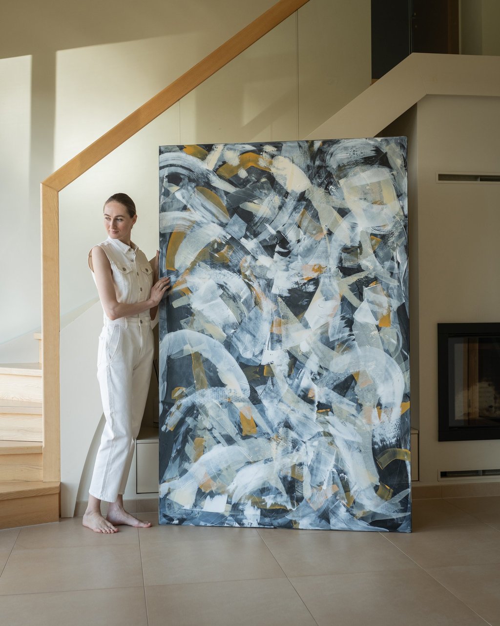 Artist standing next to a large abstract expressionist painting featuring black, white, and gold brushstrokes.
