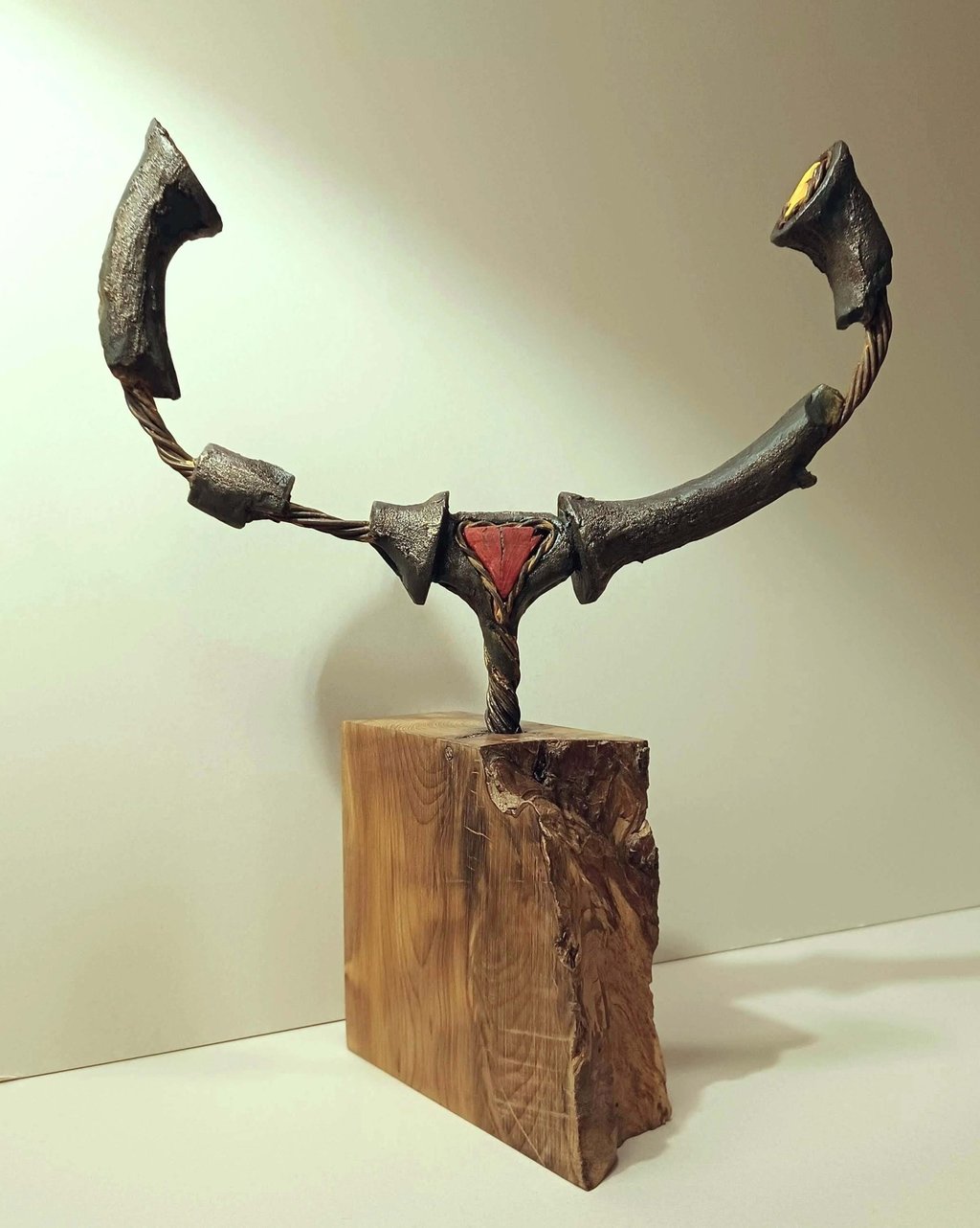 A semi circular, linear sculpture, painted bronze with red and yellow details, on yew plinth.