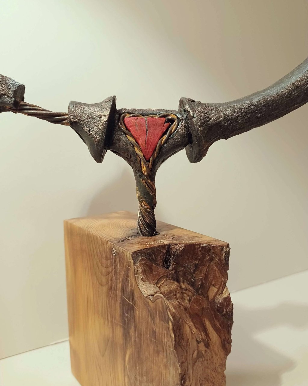 Close up of a semi circular, linear sculpture, painted bronze with red detail, on yew plinth.