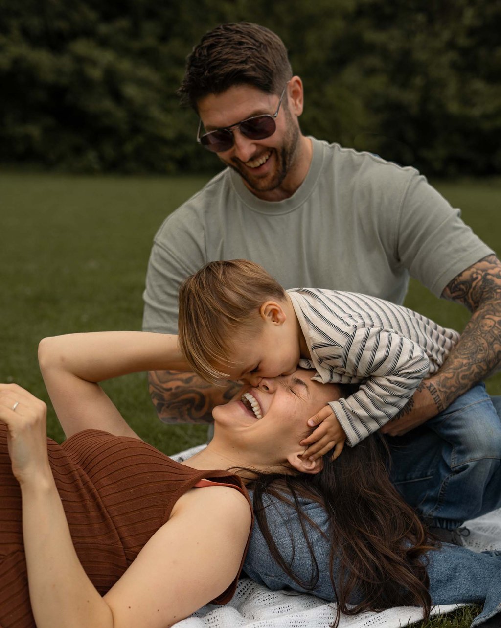 Mother lying on the grass and laughing her son is kissing her nose