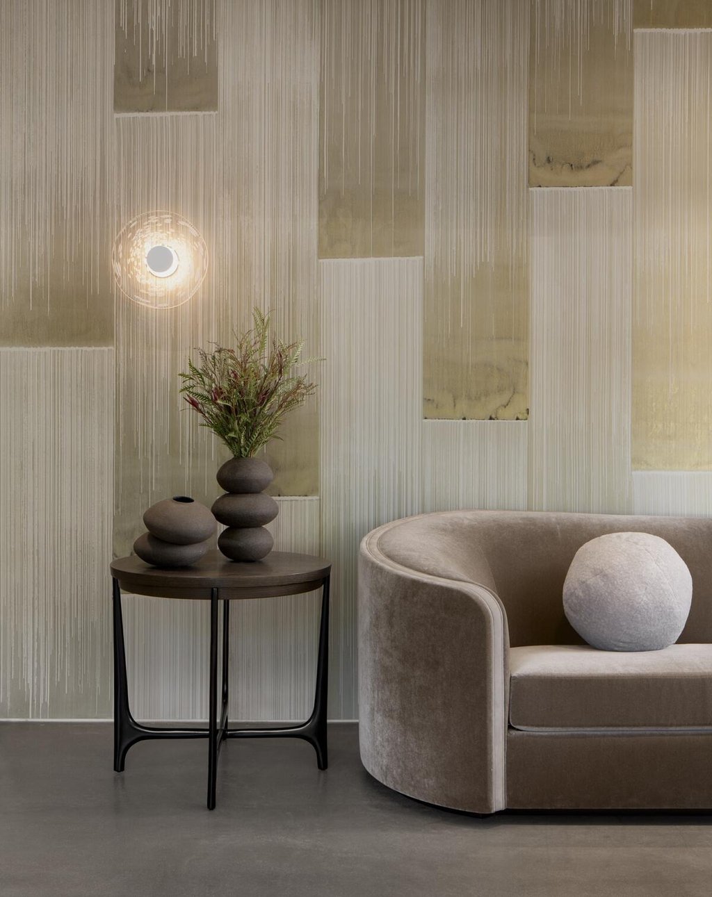 Modern living room featuring a velvet sofa, marble side table with ceramic vases, and textured wallpaper.