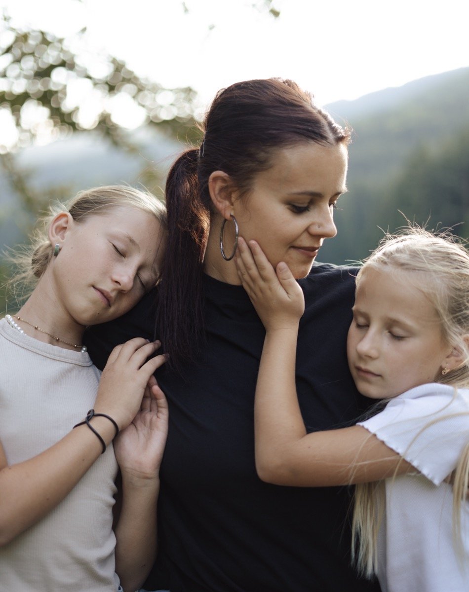 Mother holding her two daughters and smiling while her daughters are with closed eyes
