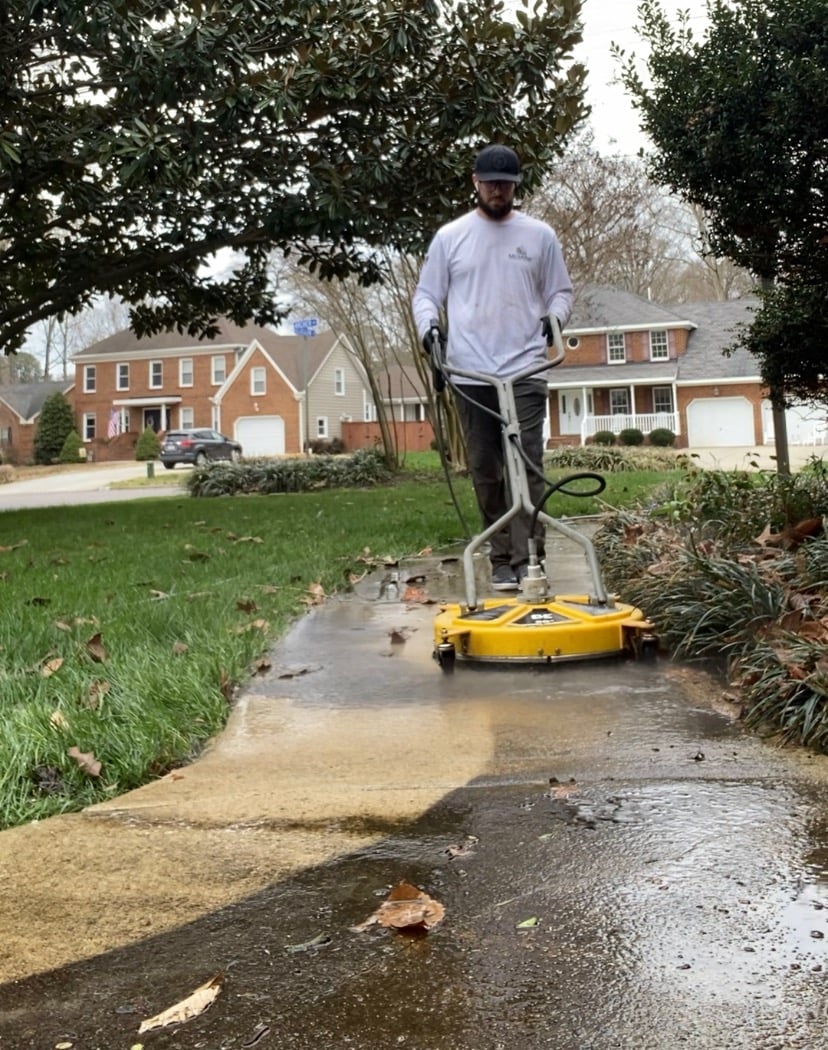 Professional pressure washing service cleaning a residential concrete sidewalk with a surface cleaner.