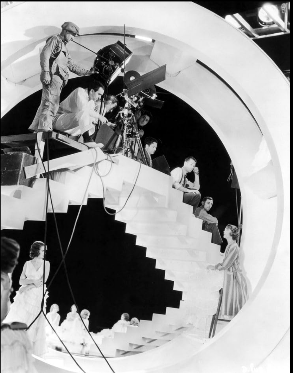 Busby Berkeley on a tall filming platform with cameras and lights, directing dancers below.