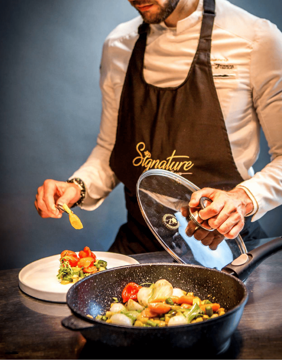 A man in a chef's apron preparing food using Napoleon Imperial Stone Noire cookware