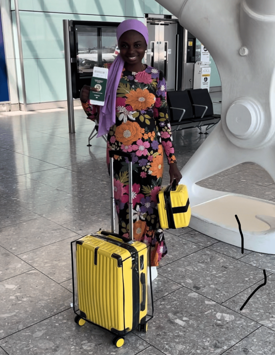 A Nigerian girl wearing a colourful dress,  holding a Nigerian passport in an airport in London