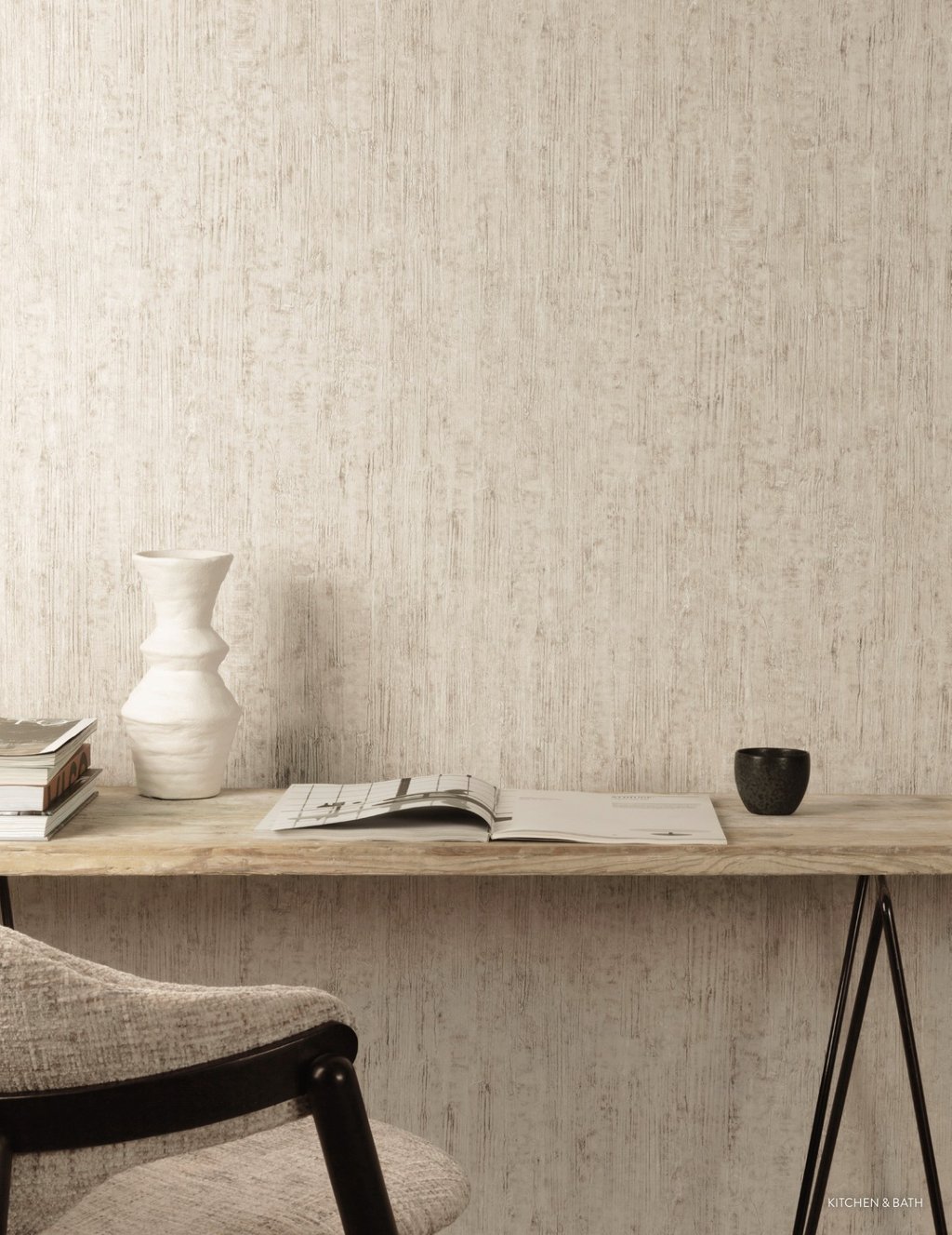 Minimalist home office with textured beige wallpaper, a wooden desk, white ceramic vase, and open book.