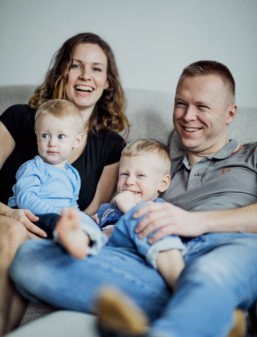 Kobieta i mężczyzna siedzą na kanapie z dwójką chłopców. Śmieją się.