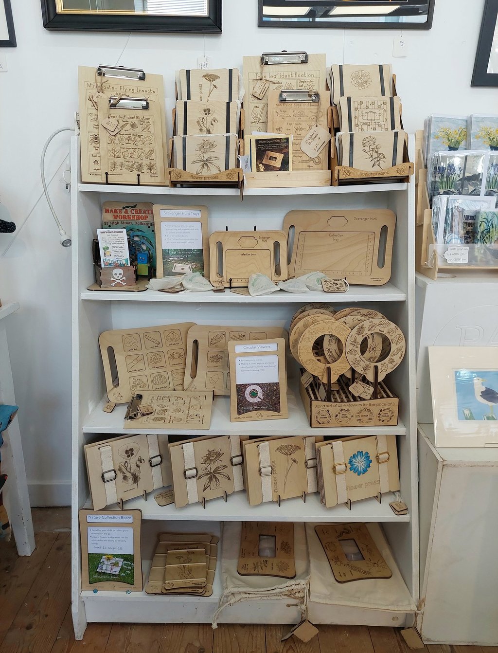 Dalbeattie Wood product display on white shelving unit. Wooden flower presses, clipboards, scavenger hunt boards