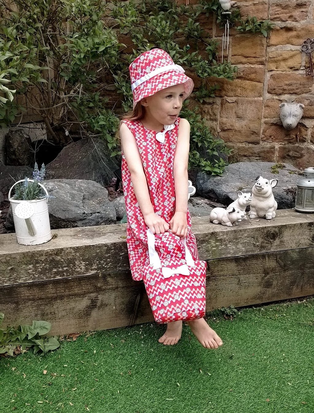 Young girl wearing a handmade a red dress with matching hat and bag made in Nottingham UK from sustainably sourced fabric