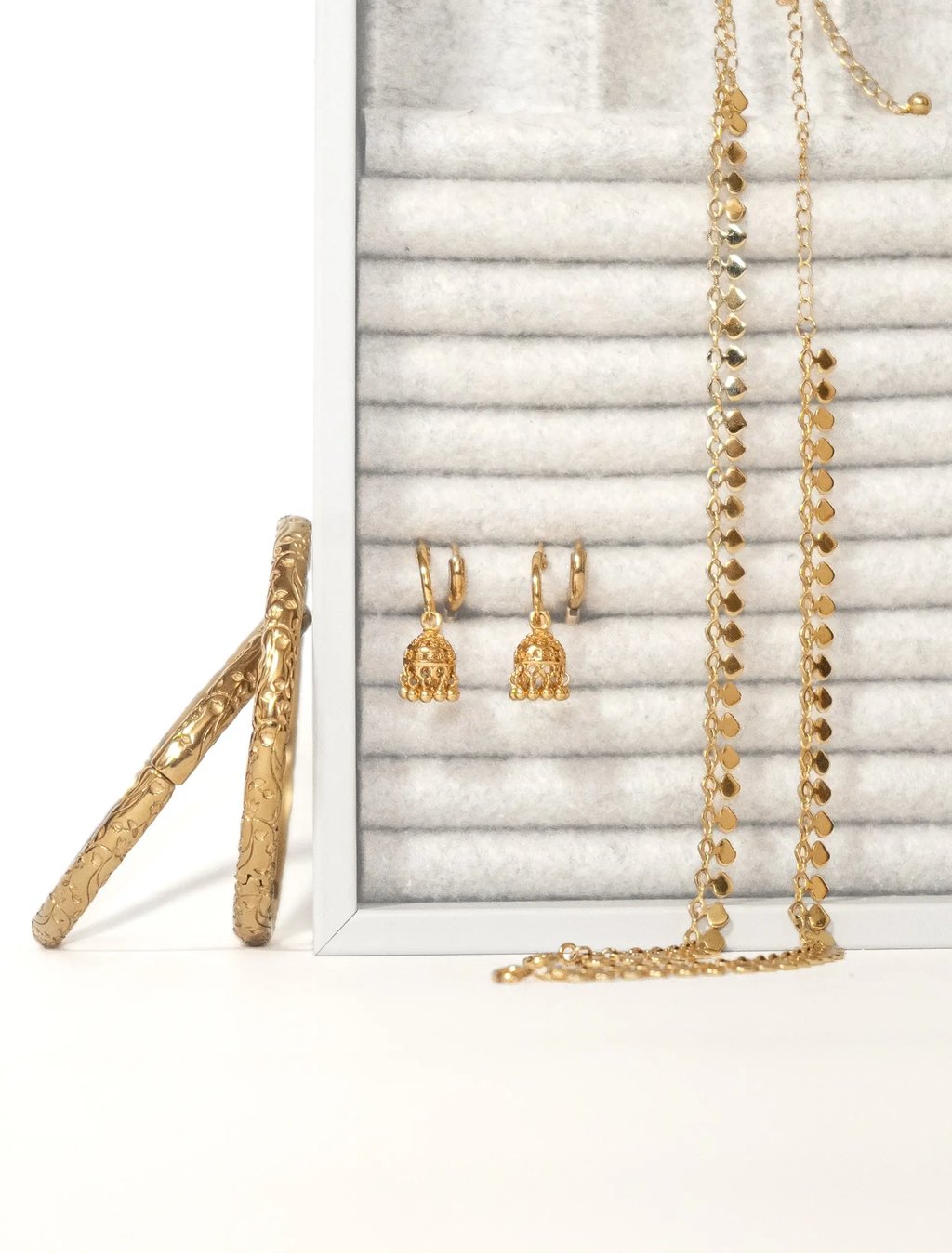 Gold jewellery collection arranged on a white display with earrings and layered anklets