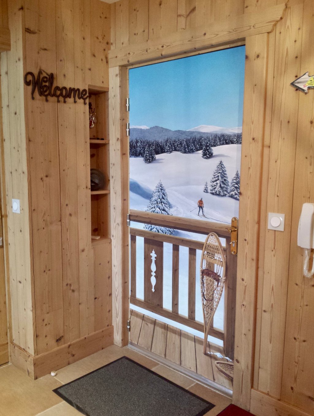 Hall d'entrée avec trompe-l'oeil sur porte d'entrée. Paysage neige, skieur, raquettes neige, bois