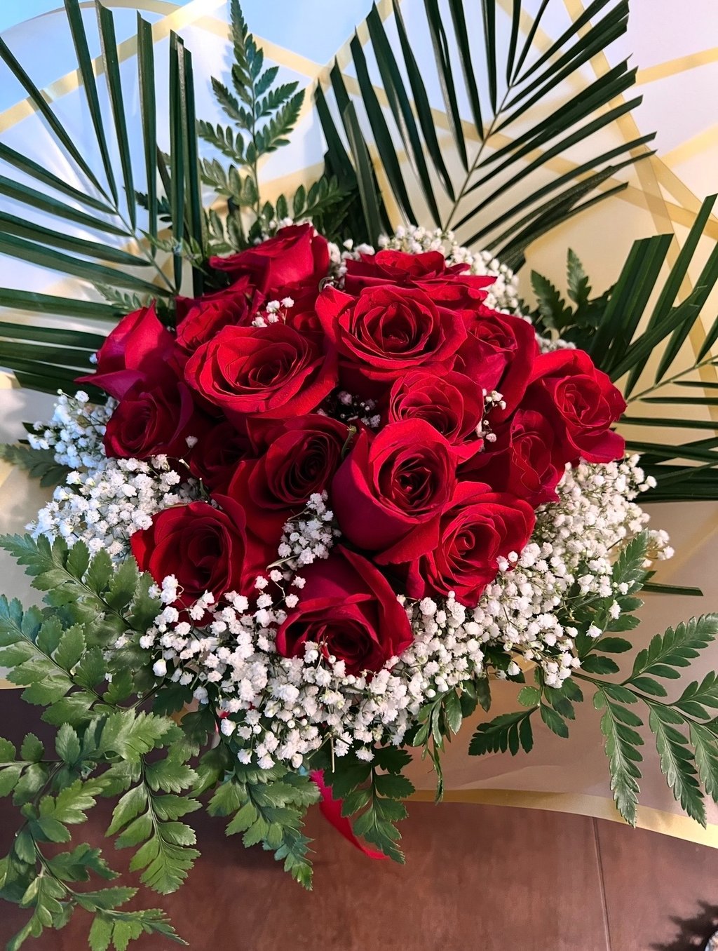 A bouquet of fresh red roses and white baby's breath flowers with green palm leaf accents.