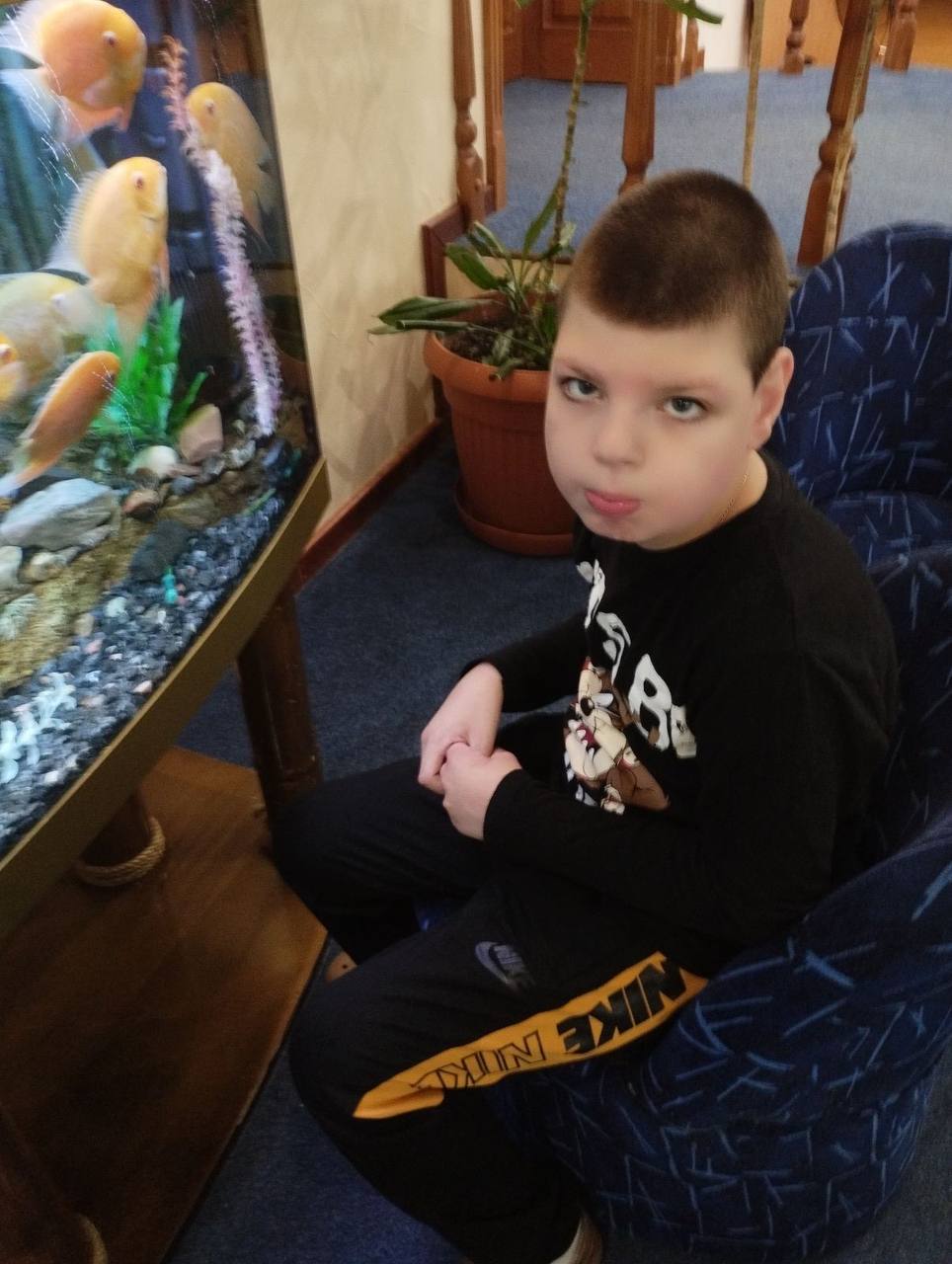 молодий хлопчик сидить у кріслі з акваріумом