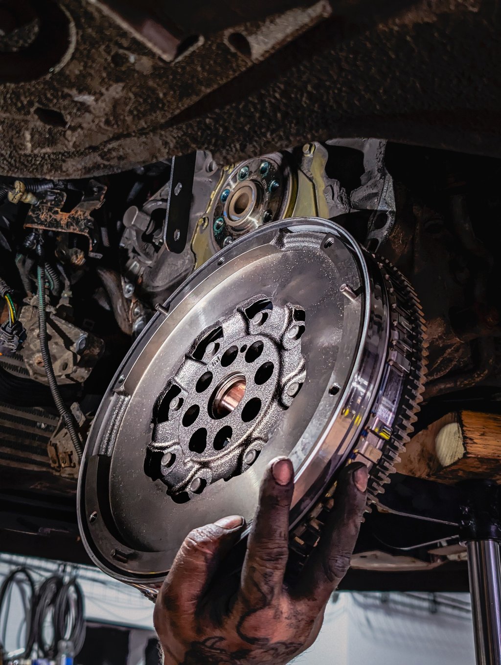 A mechanic holding a high-performance steel flywheel during a car engine and clutch repair.