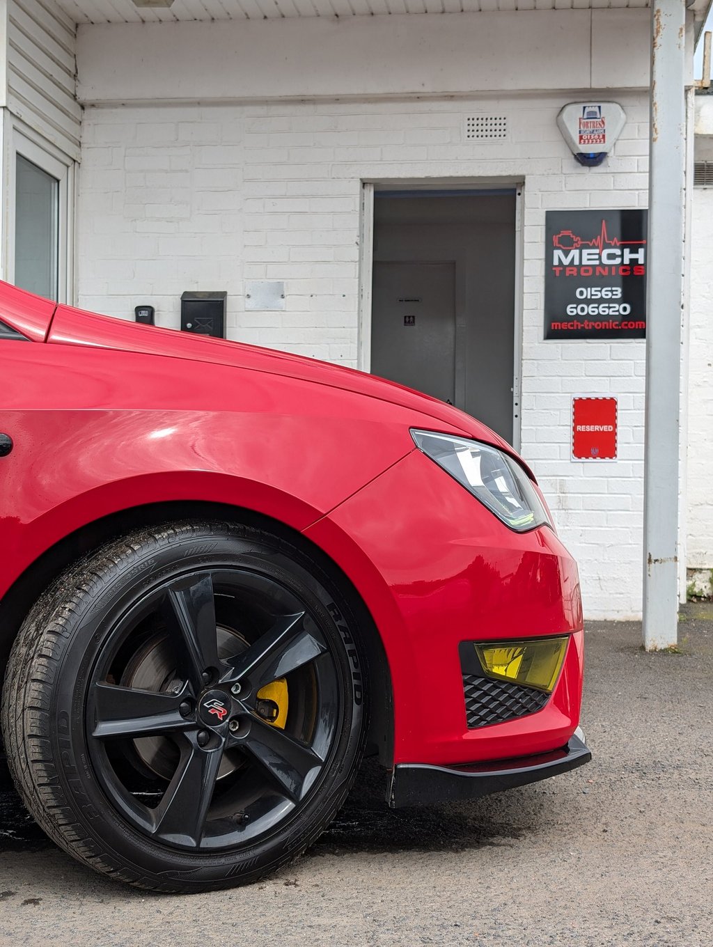 Red Seat Ibiza with black alloy wheels parked outside a Mech Tronics automotive repair shop.