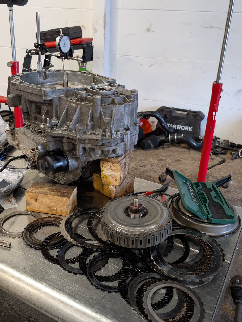Disassembled car transmission with gears and clutch plates on a workbench for repair.