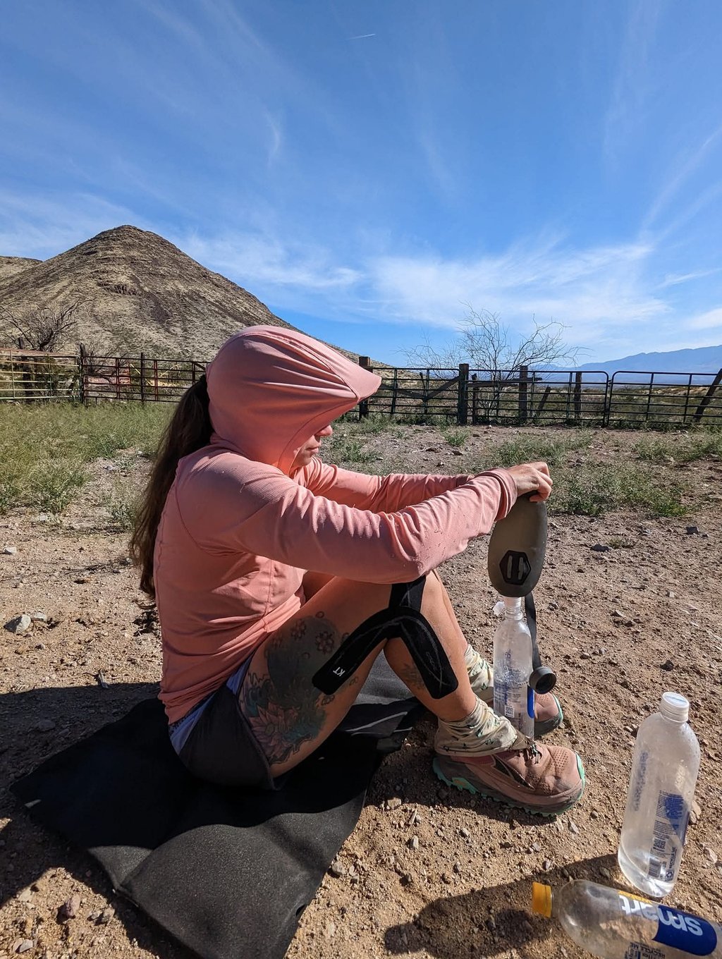 Samantha in a pink sun hoodie filters water in a Hydrapak seeker bladder in the New Mexican desert.
