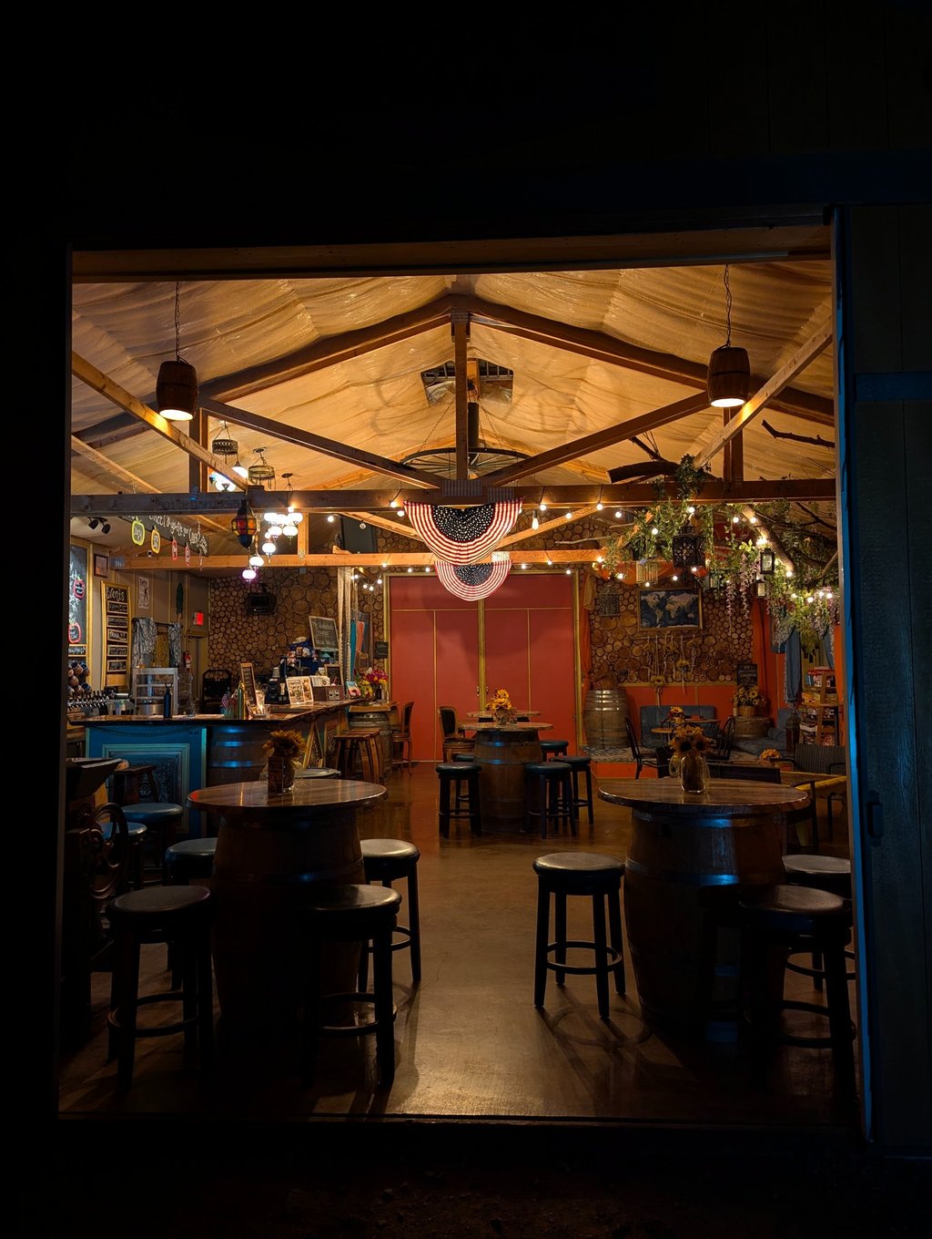 Rustic interior of a craft brewery taproom featuring wooden barrel tables, bar stools, and warm ambient lighting.