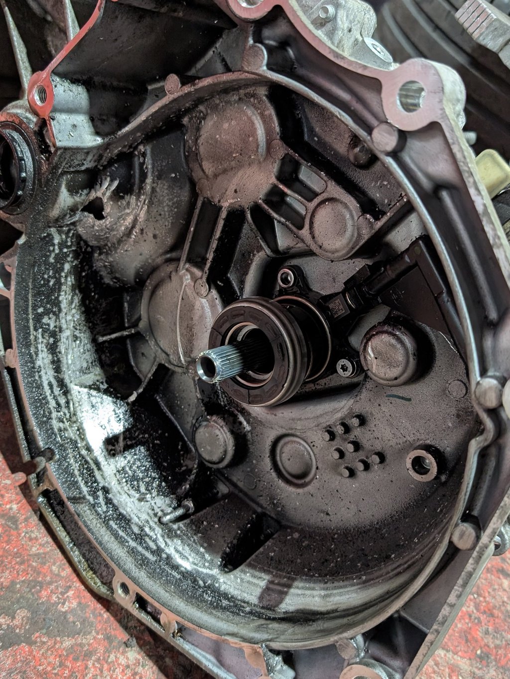 A grease-covered automotive transmission bell housing with an input shaft and release bearing.