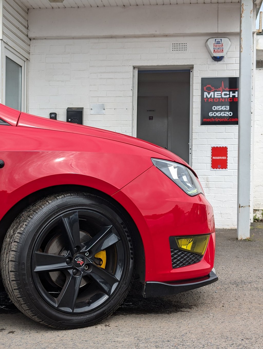 Red Seat Ibiza with black alloy wheels parked outside a Mech Tronics automotive repair shop.