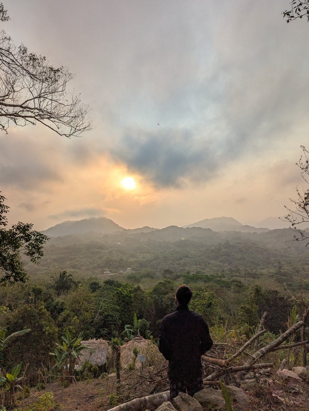 A hiker looking at a scenic mountain sunrise over a lush tropical jungle valley.