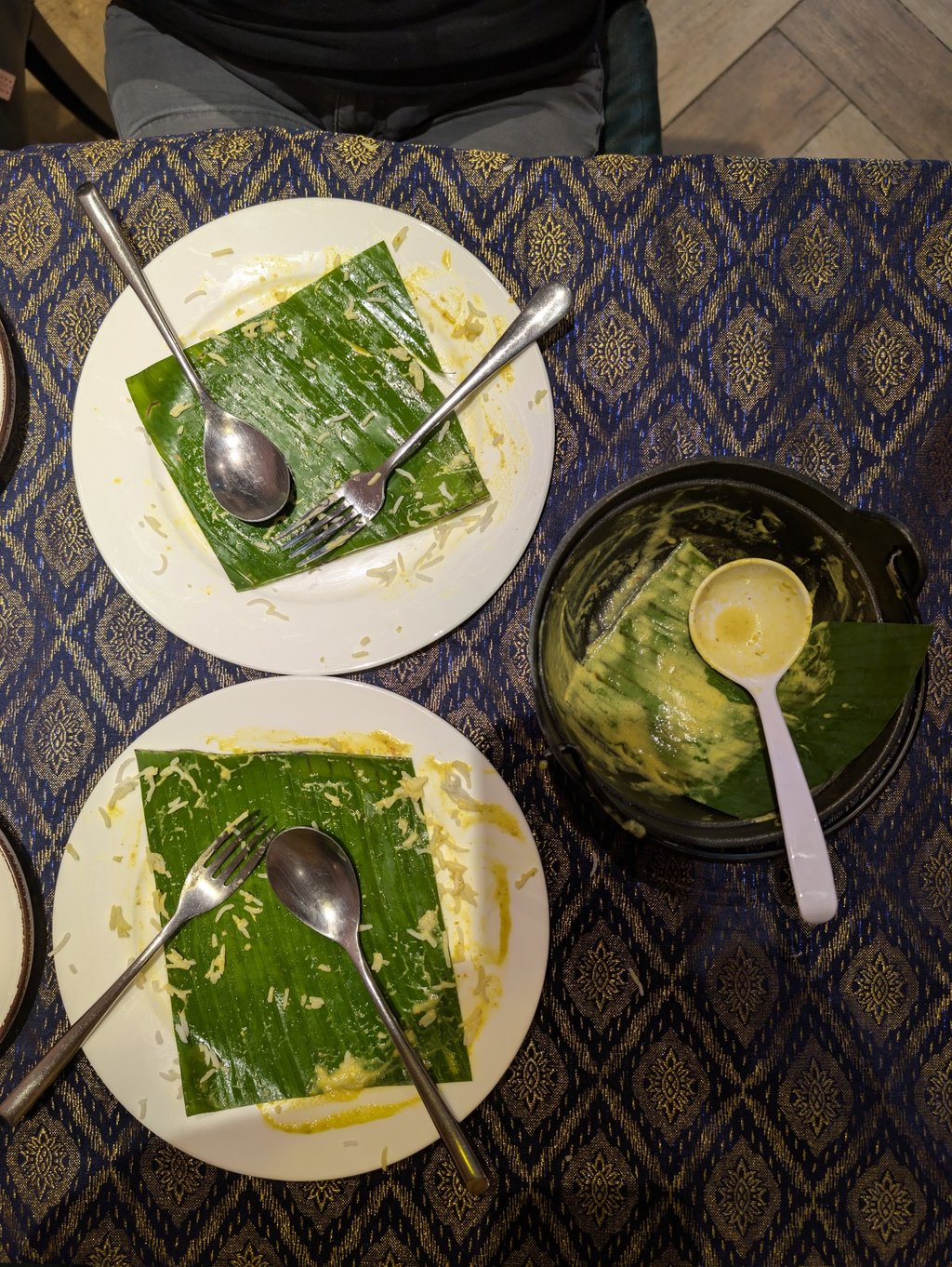 Empty plates with banana leaves and silver cutlery after a traditional Southeast Asian meal.