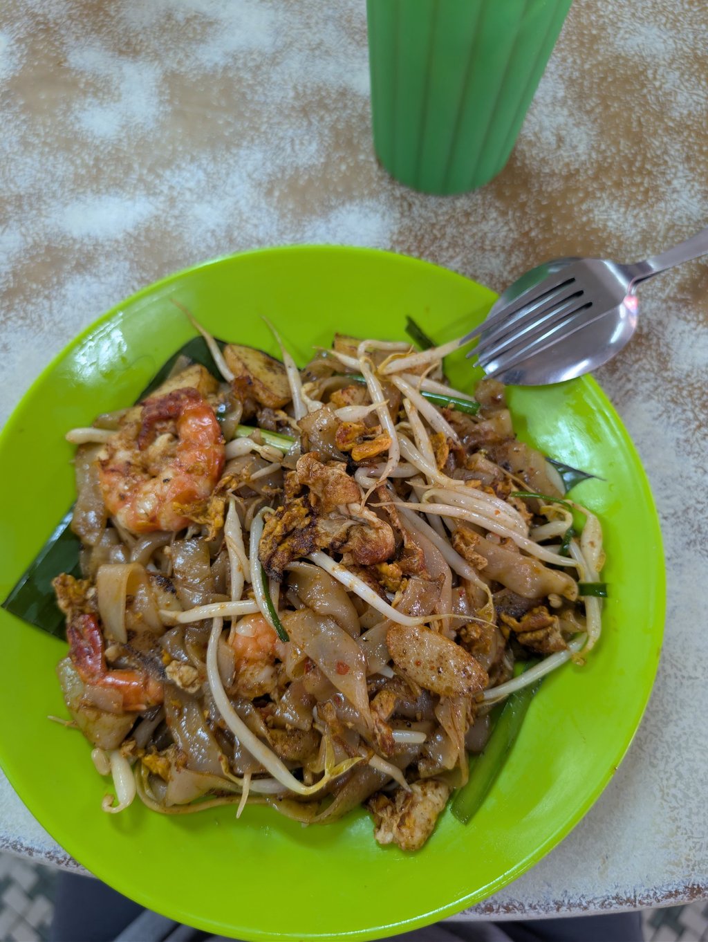Authentic Char Kway Teow stir-fried rice noodles with prawns and bean sprouts on a green plate.