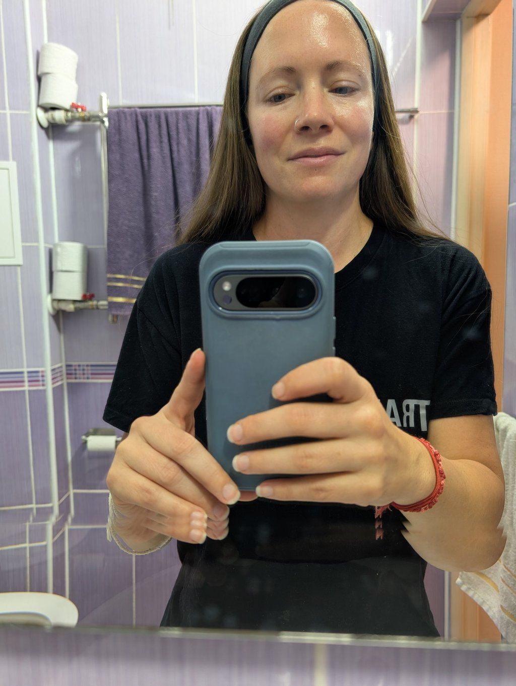 A woman with glowing skin taking a mirror selfie in a purple tiled bathroom after skincare 
