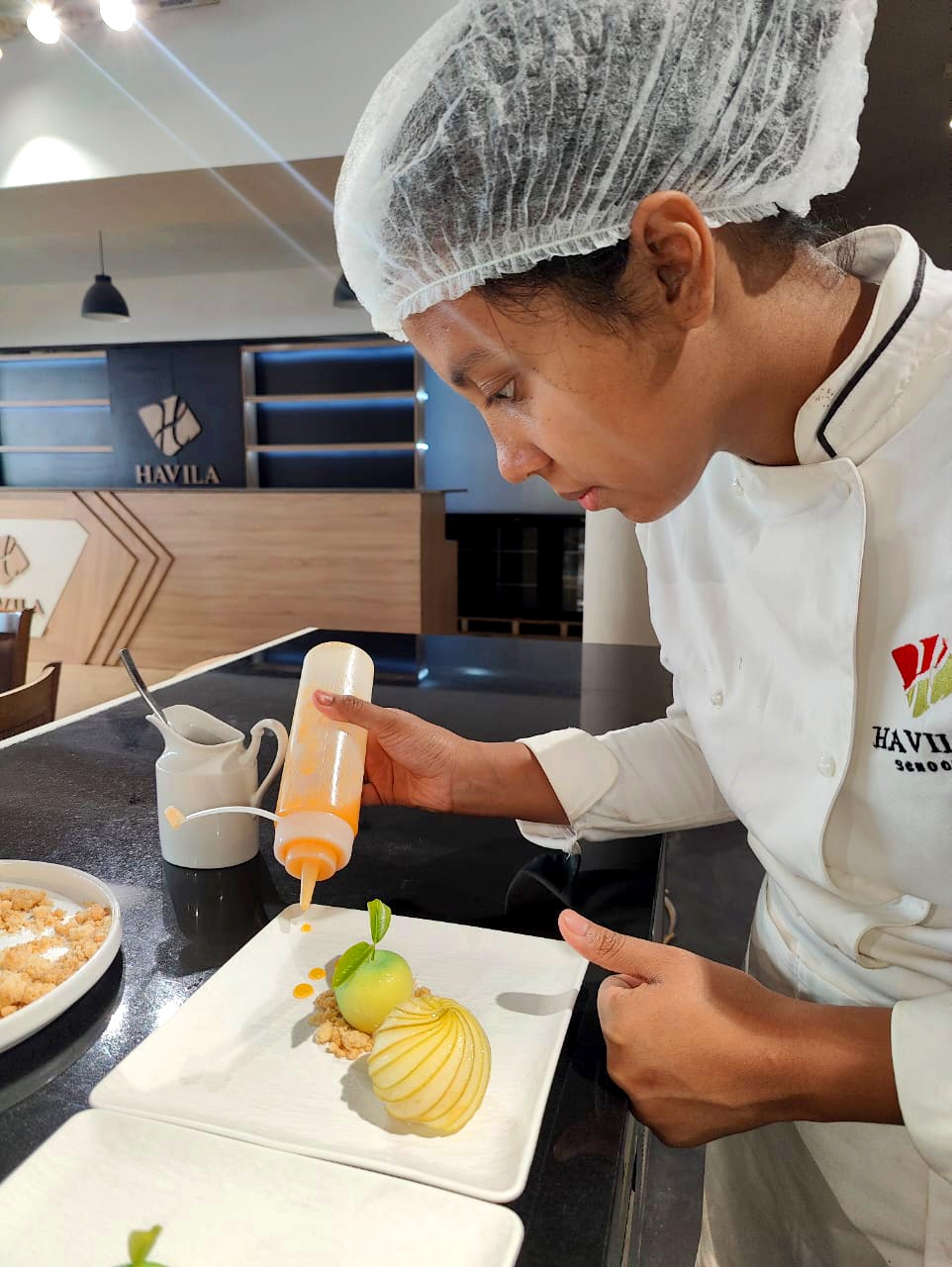 a chef in a white uniform is pouring a sauce on a plate