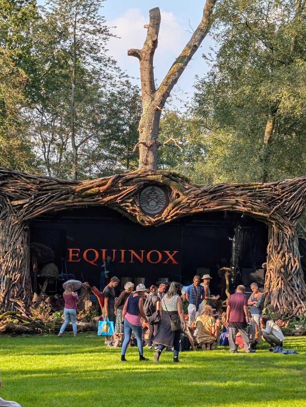 Crowd gathered at the Equinox outdoor festival stage featuring a unique rustic tree root archway.