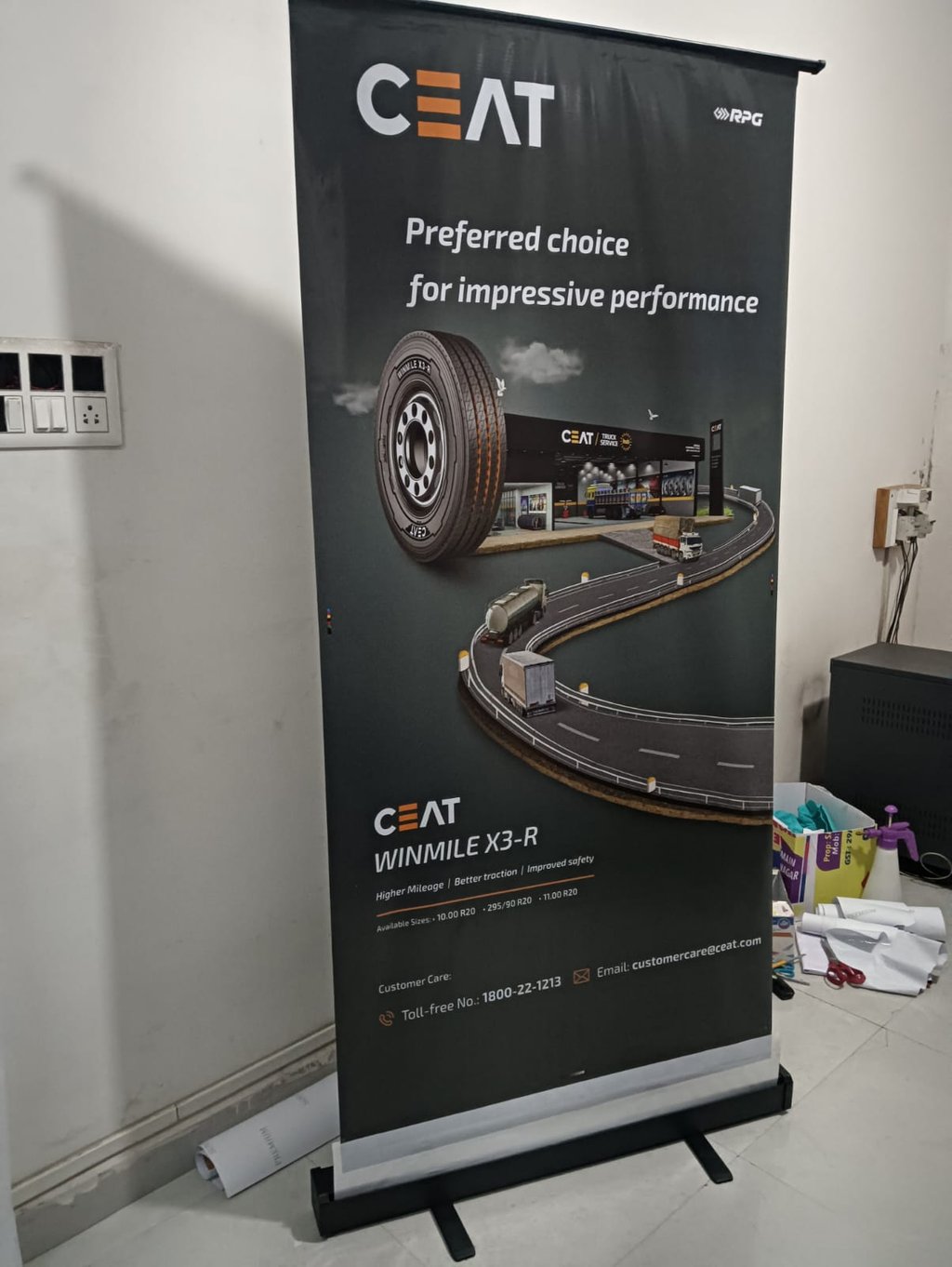 CEAT Winmile X3-R truck tire advertisement on a vertical banner stand in an indoor office setting.
