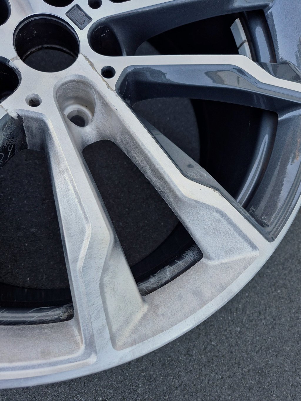 Close-up of a damaged alloy car wheel rim with visible curb rash and surface scratches.