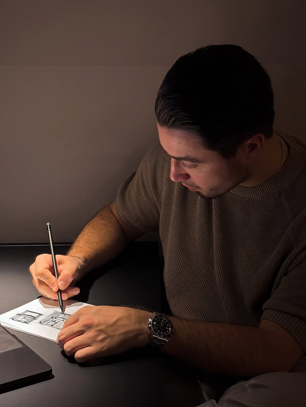 A designer sketching with a pencil at a dark desk.