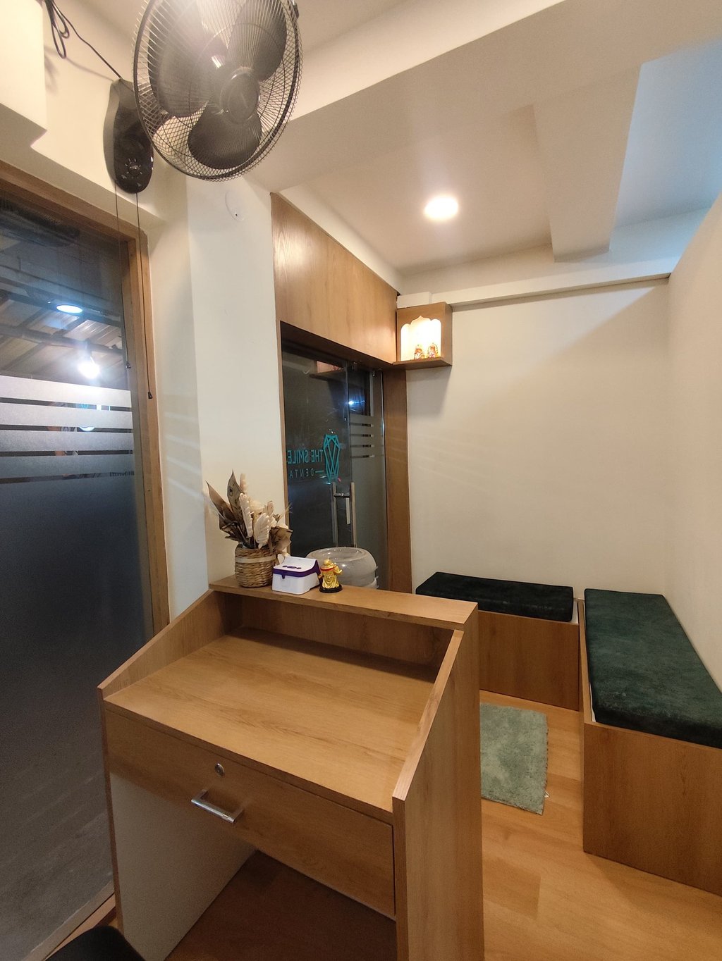 A modern dental clinic reception area featuring a wooden desk and velvet waiting room benches.
