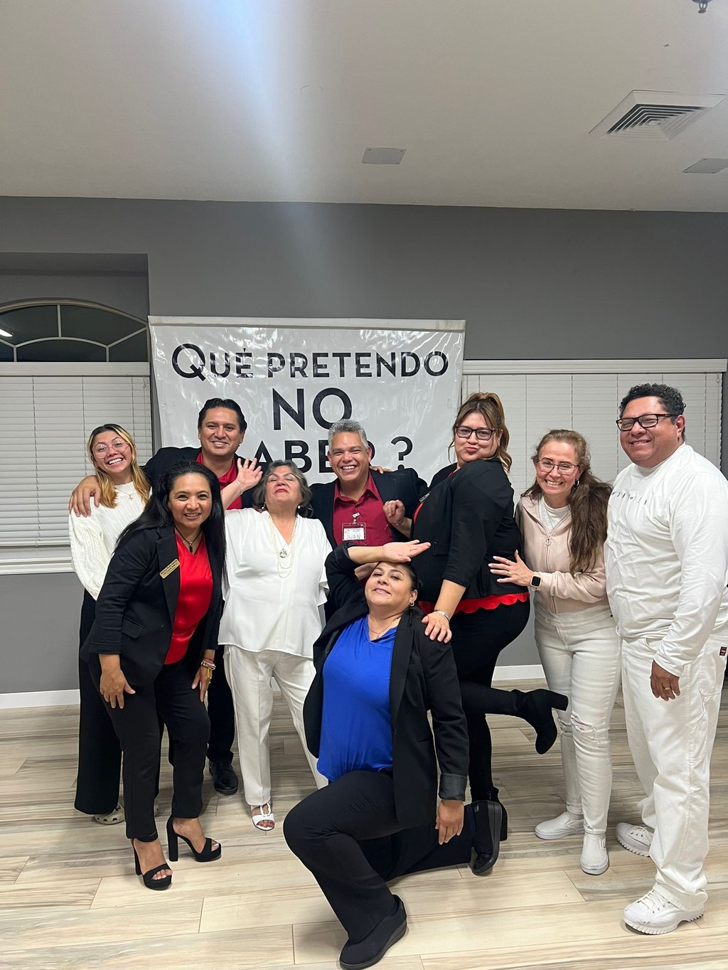 Diverse professional group posing by a Que Pretendo No Saber banner for team building.