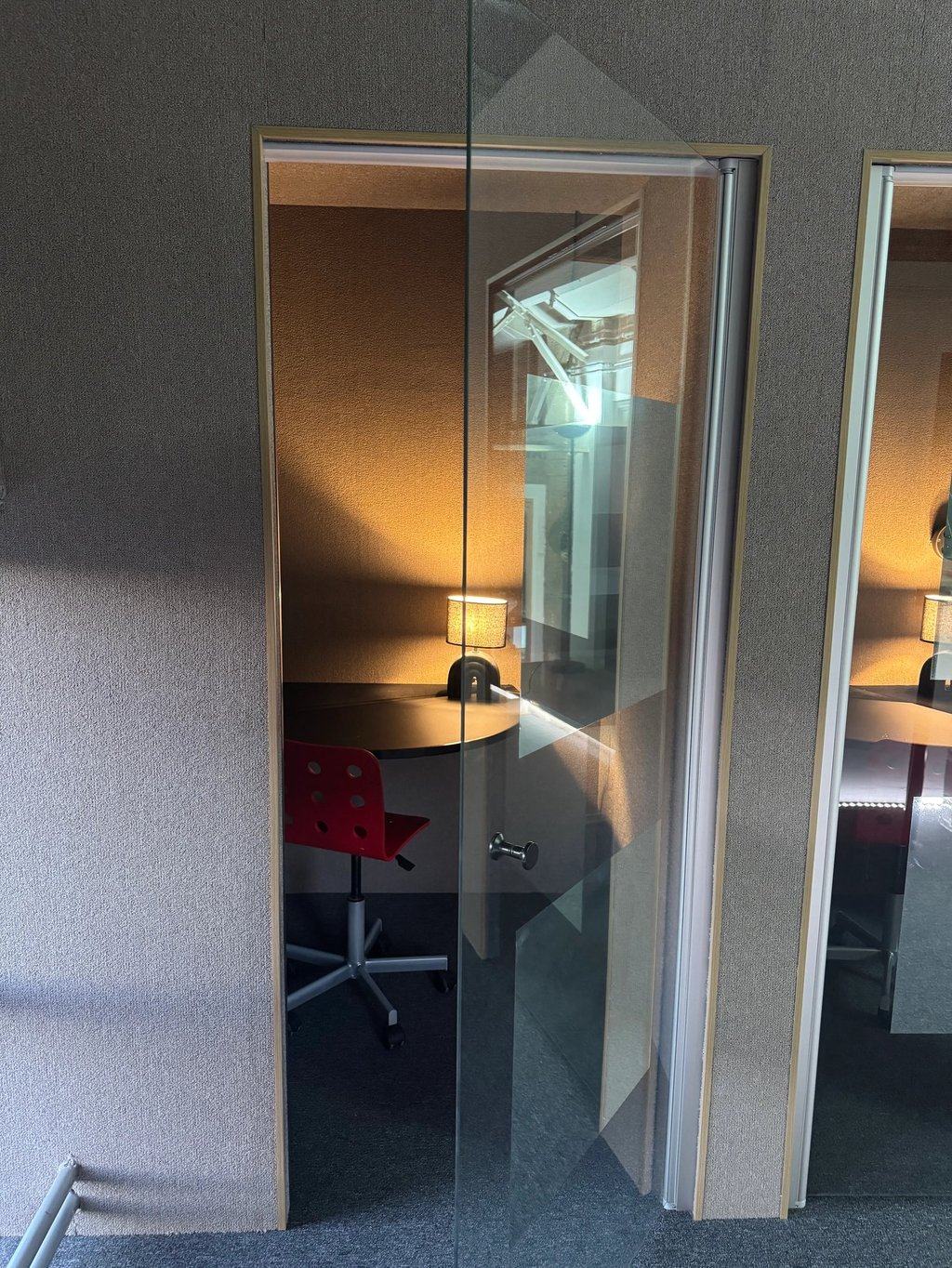 Deux cabines de bureau insonorisées avec portes vitrées, équipées d'un tabouret haut, tablette et lampe d'appoint.