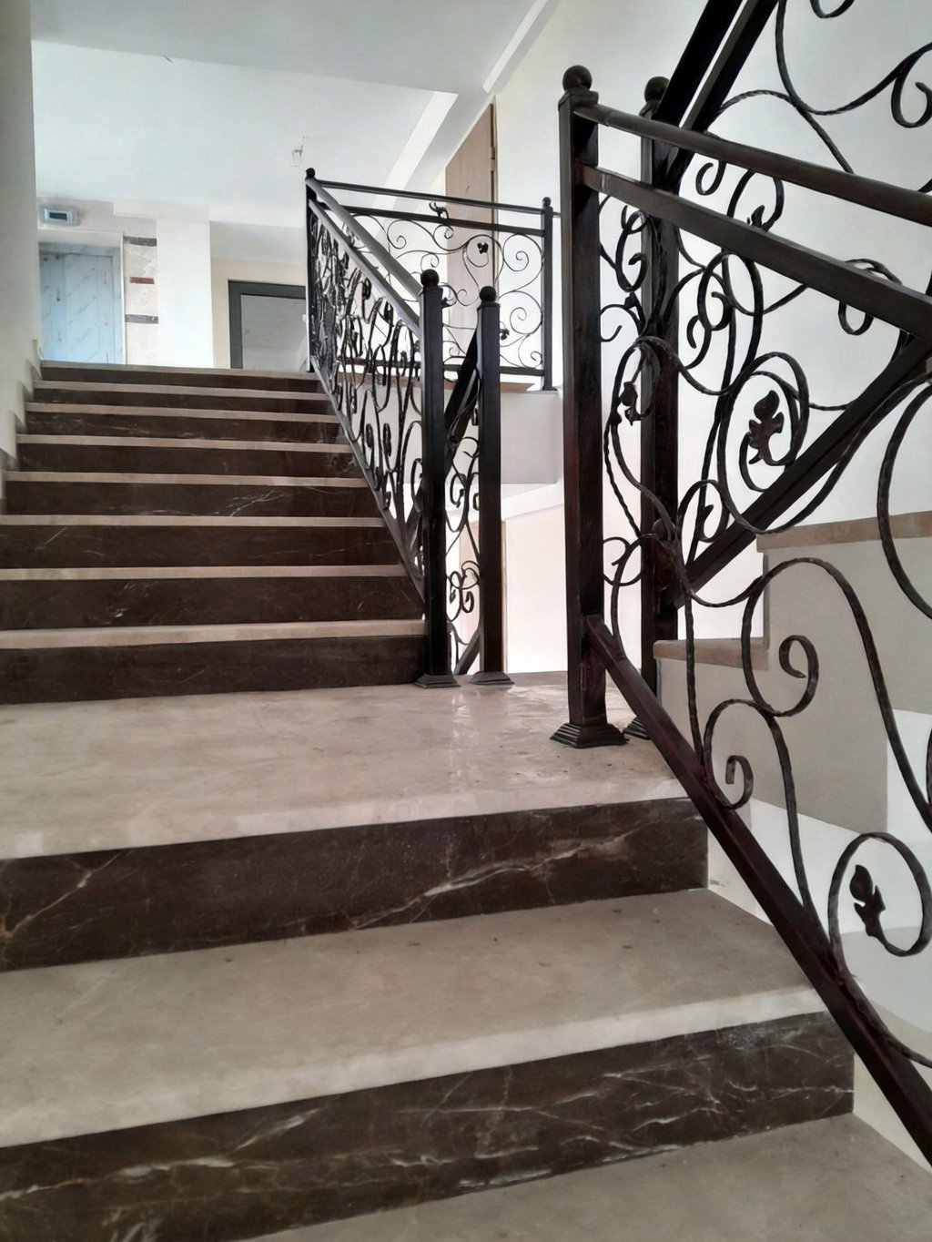 Elegant marble staircase with ornate black wrought iron handrails in a modern interior.