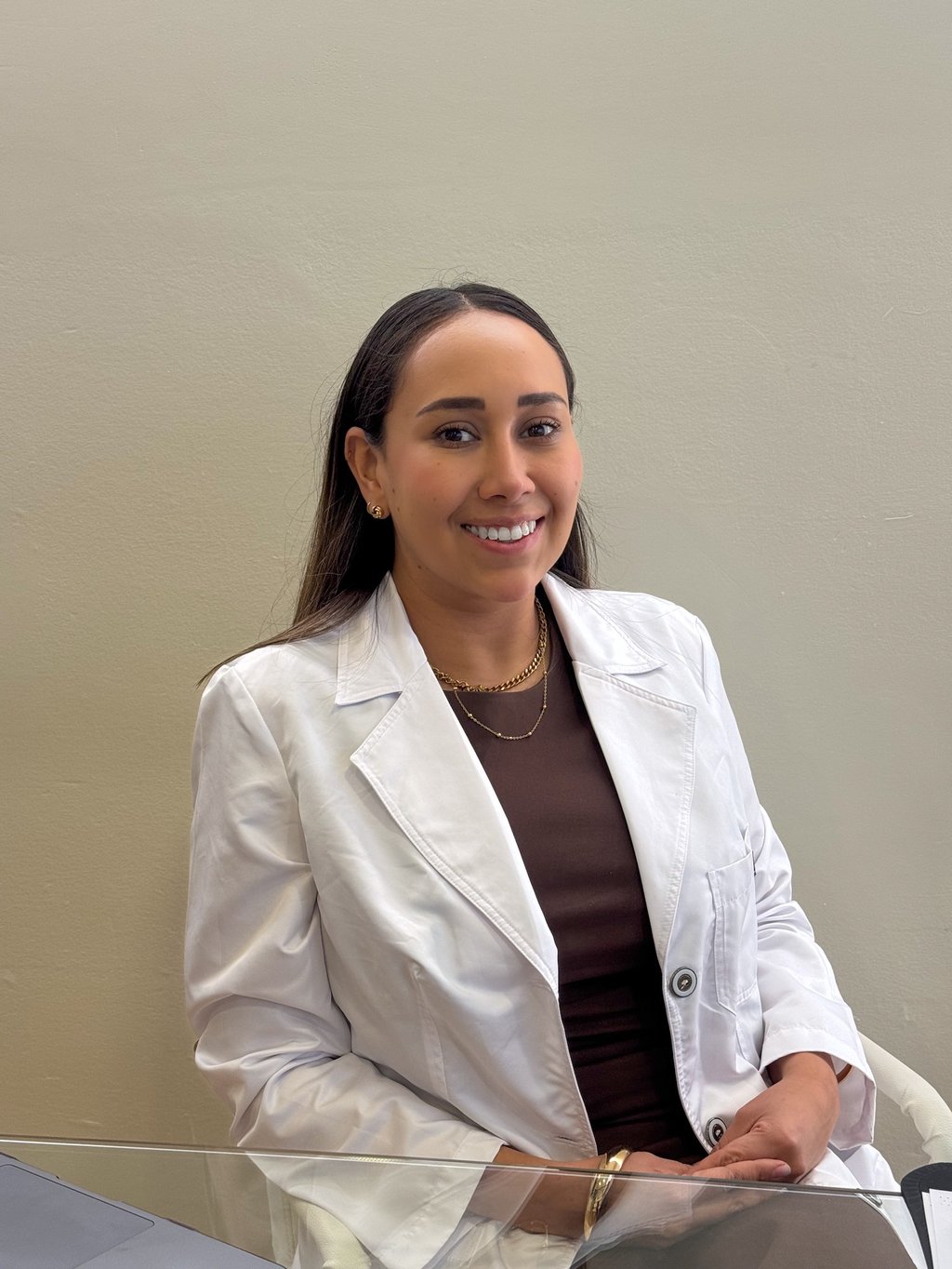 Smiling female medical professional in a white lab coat sitting at a desk.