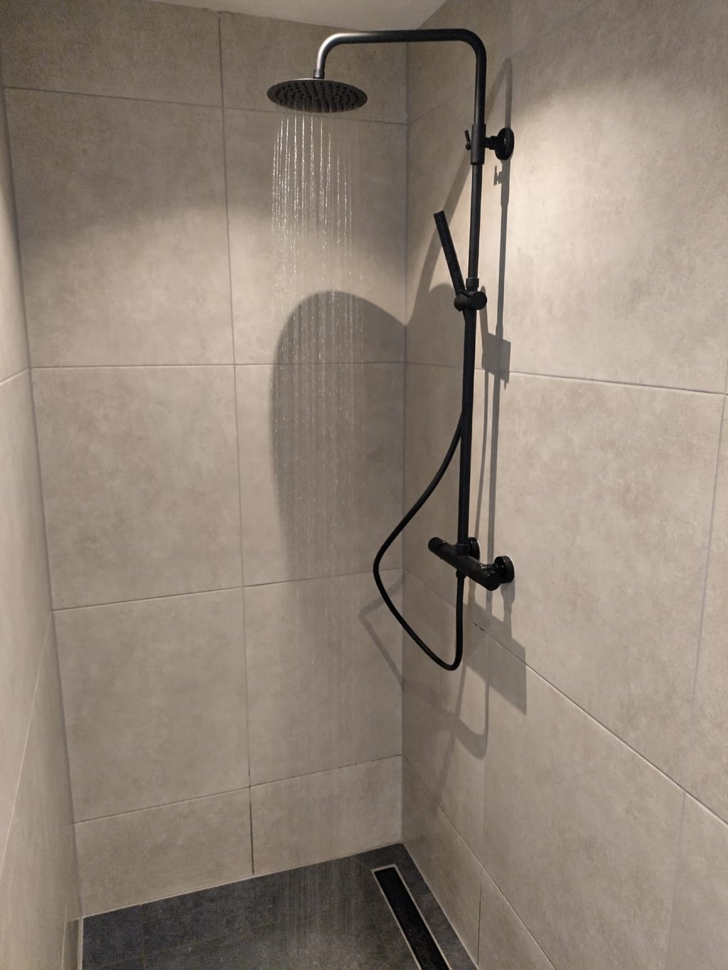 Zwarte douche in sobere badkamer met grote tegels.