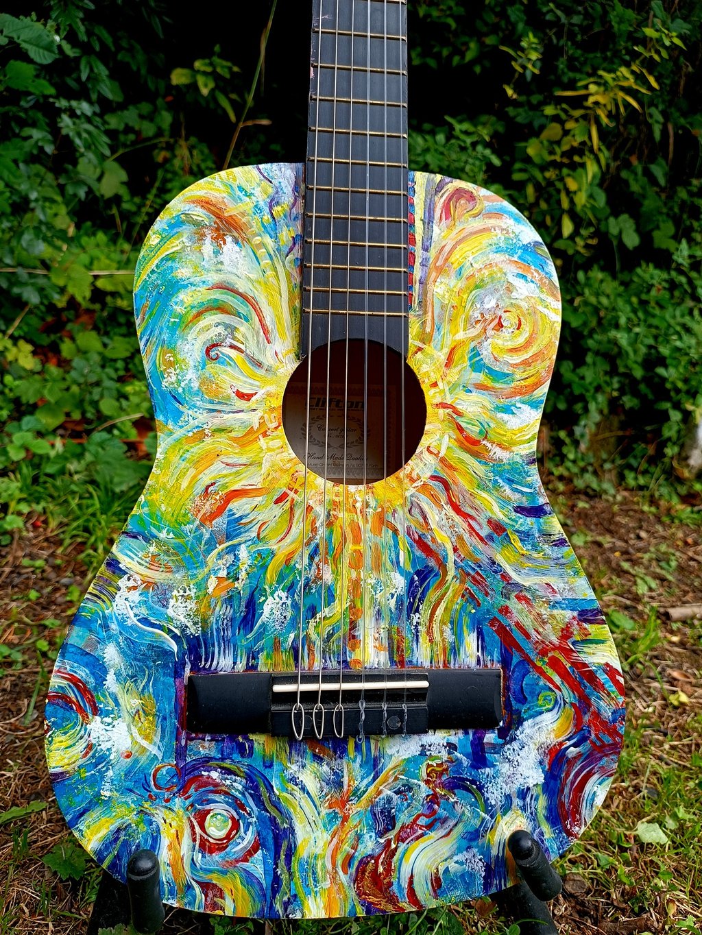 peinture sur guitare aux couleurs vives, avec un soleil autour de la rosace et des formes abstraites