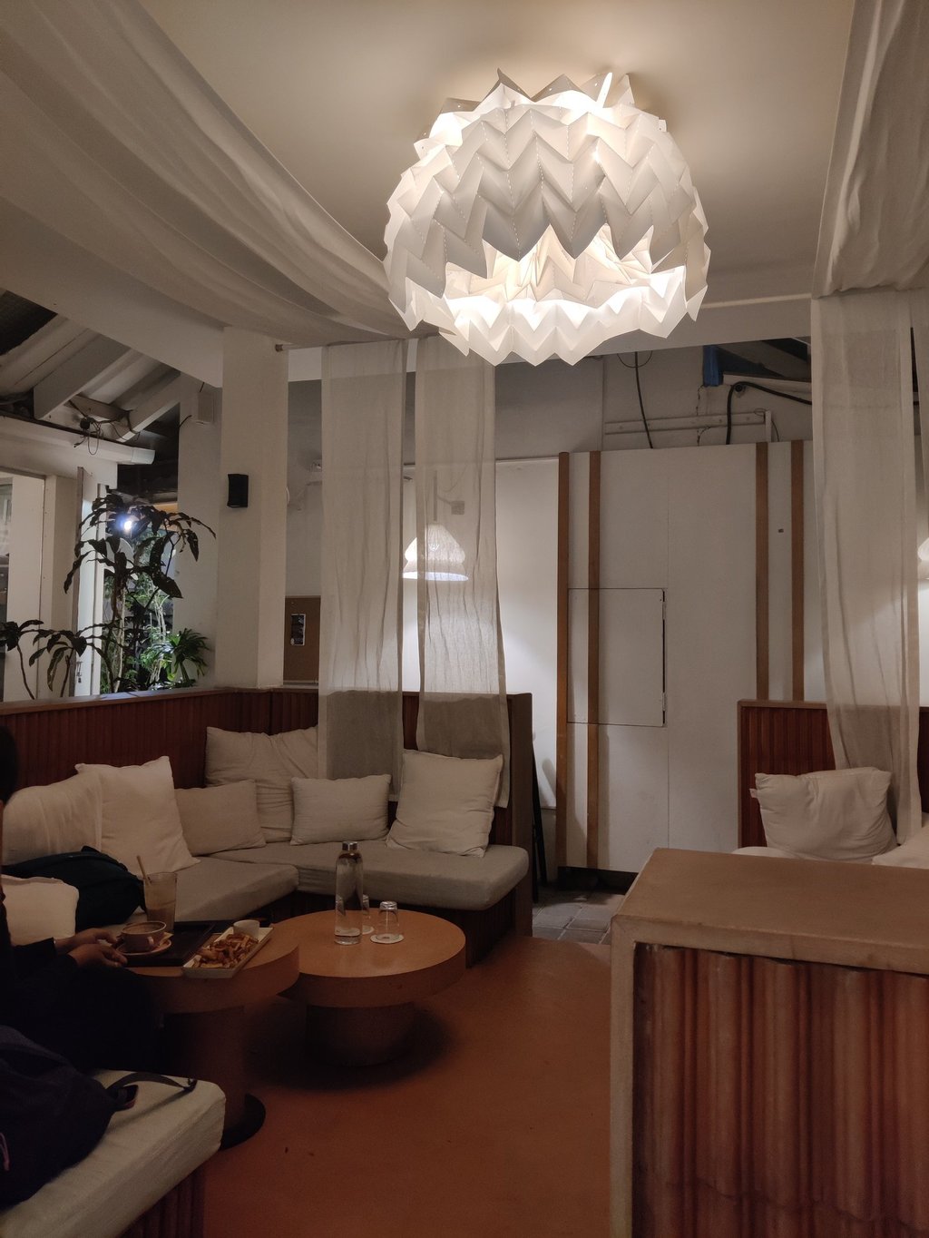 Cozy cafe interior featuring a geometric  light, white drapes, and comfortable lounge seating with pillows.