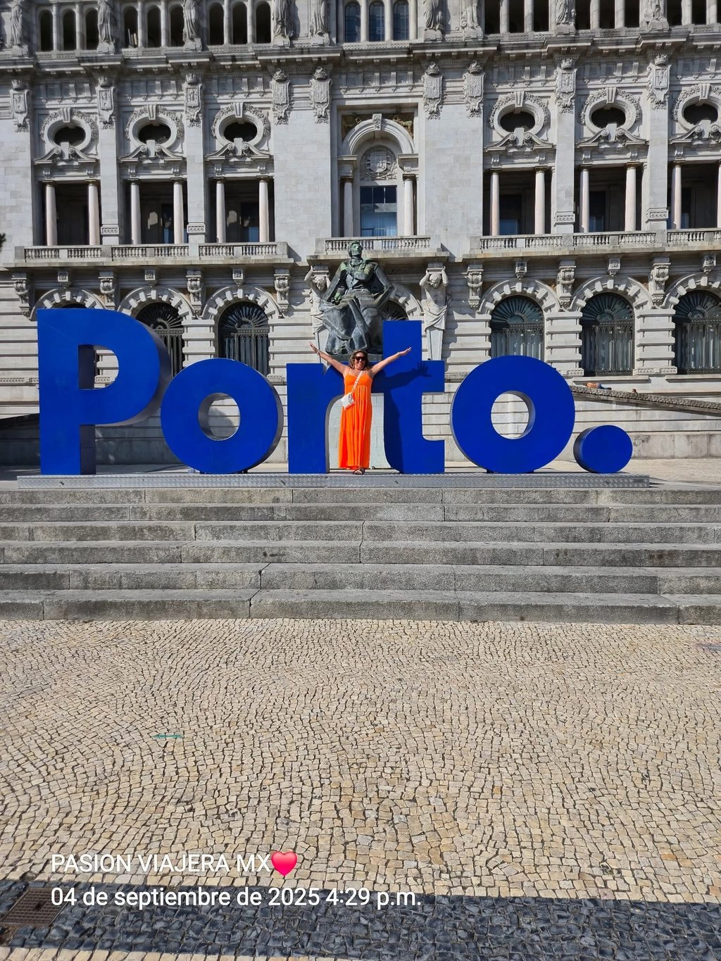Una mujer con un vestido naranja posa junto al letrero azul de Porto frente al Ayuntamiento de Portu