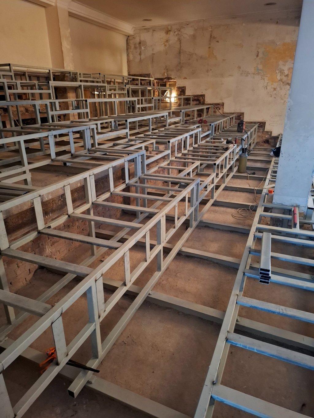 Steel tier seating frame under construction inside a renovated auditorium or lecture hall.