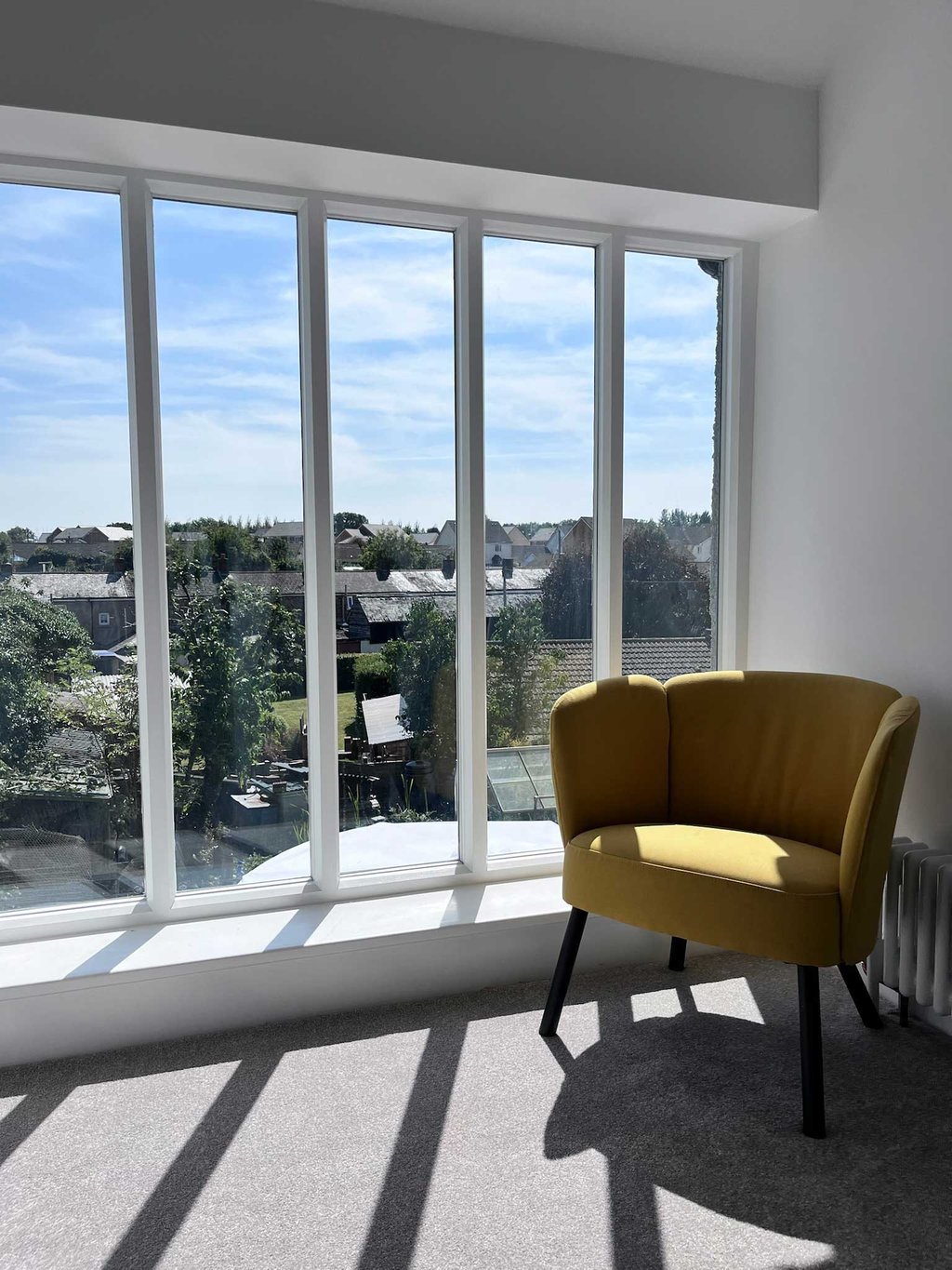 Mustard coloured chair next to large sunny window with village views