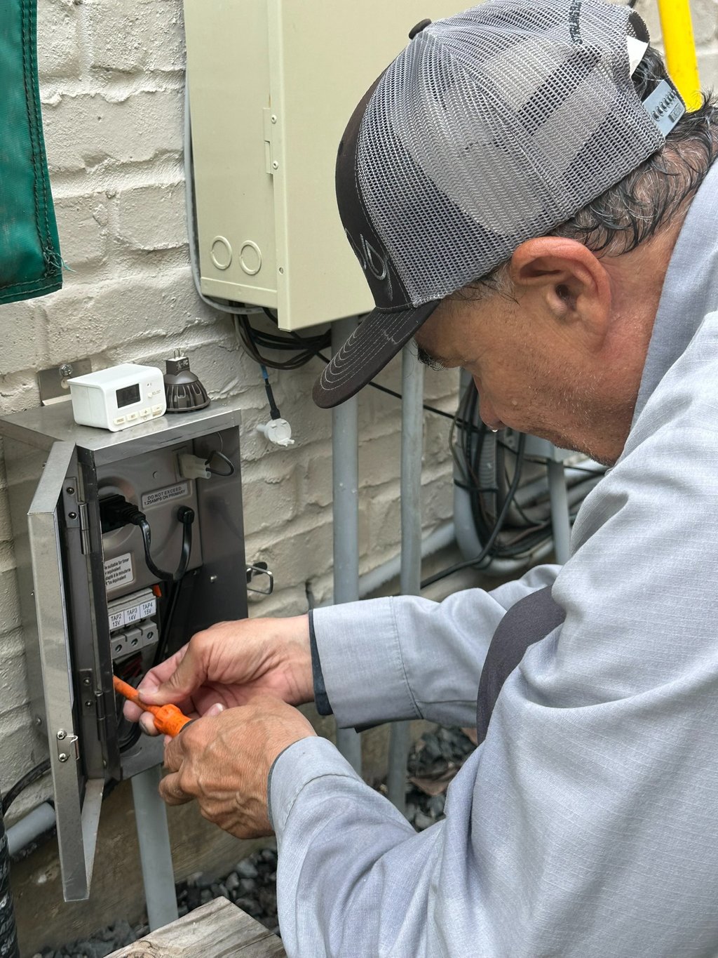 Electrician installing low voltage landscape lighting transformer for outdoor lighting system.