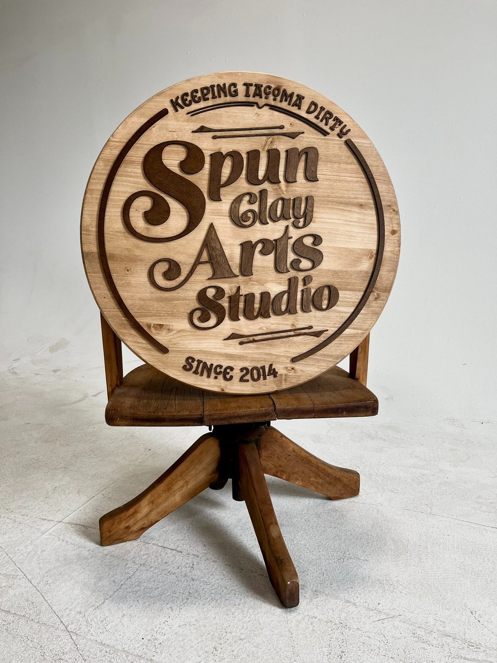 Custom wood round sign for Spun Clay Arts Studio resting on a vintage wooden pottery stool.