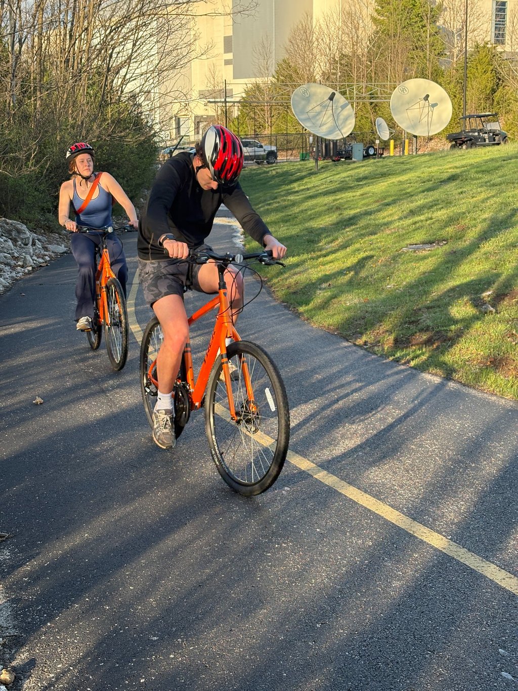 Two people on orange bikes on a paved trail